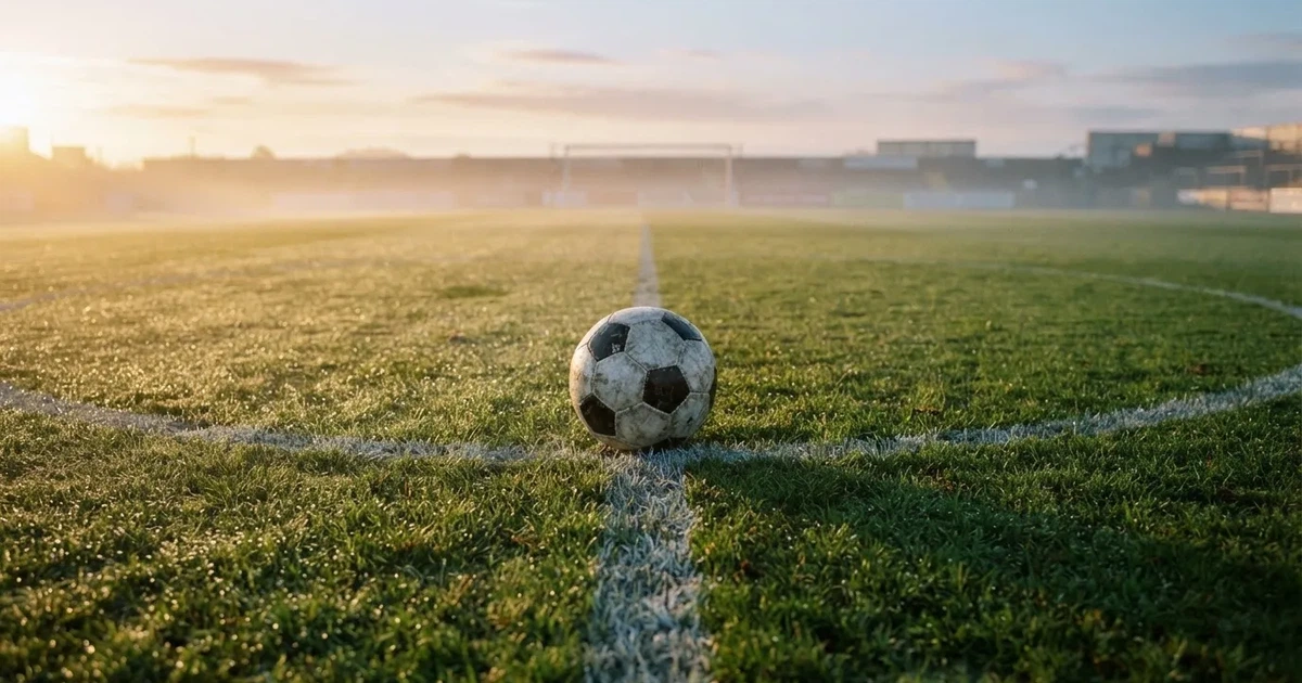 Een voetbal op de middenstip van een grasveld in het ochtendlicht
