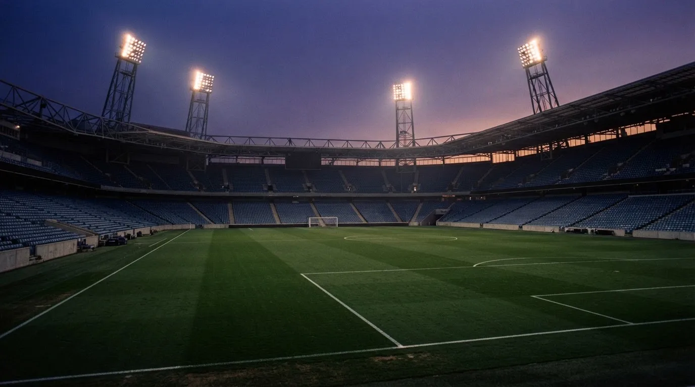 Een leeg voetbalstadion met lichtmasten bij schemering