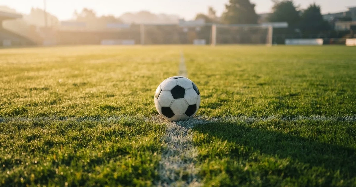 Een voetbal op de middenstip van een grasveld in het ochtendlicht