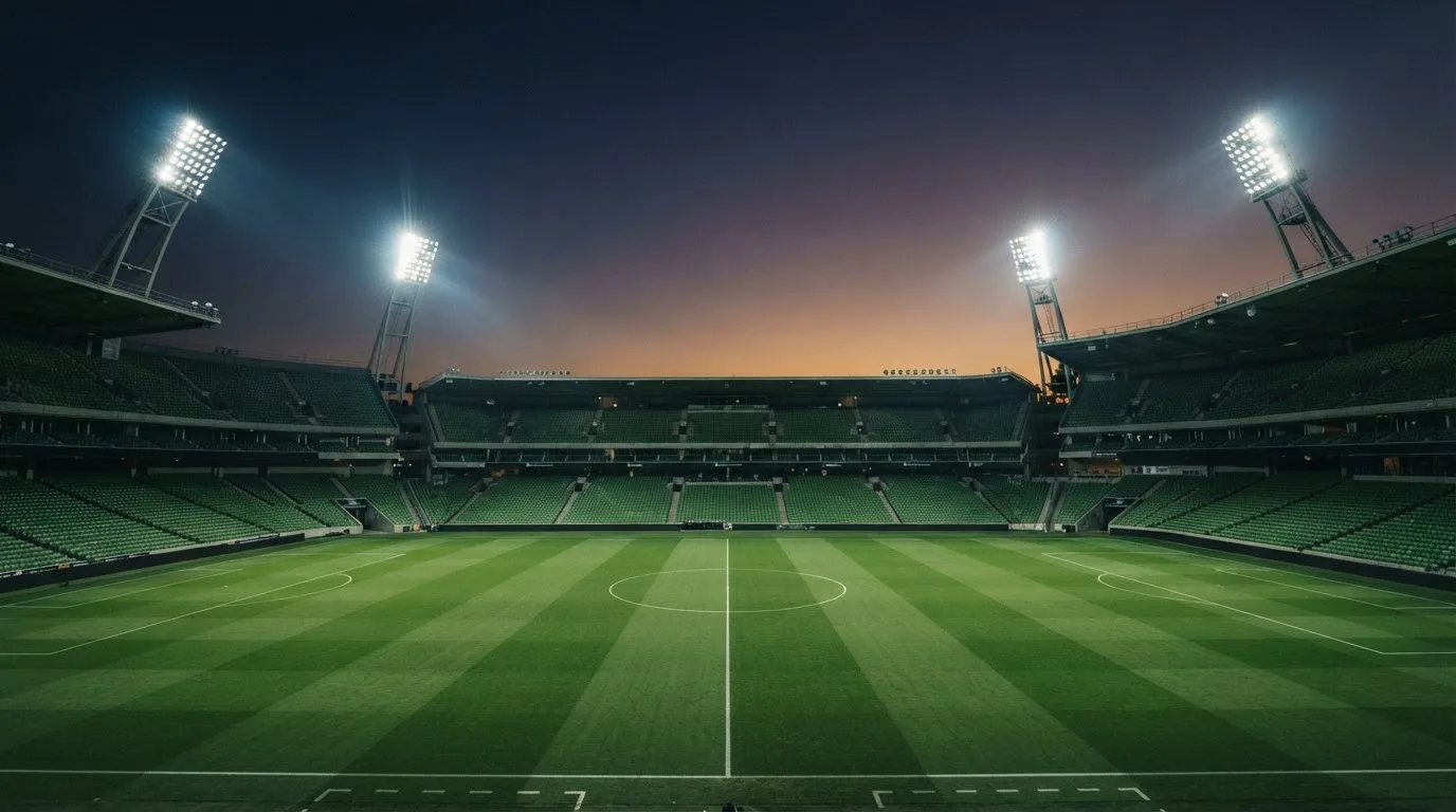 Een leeg voetbalstadion met lichtmasten bij schemering