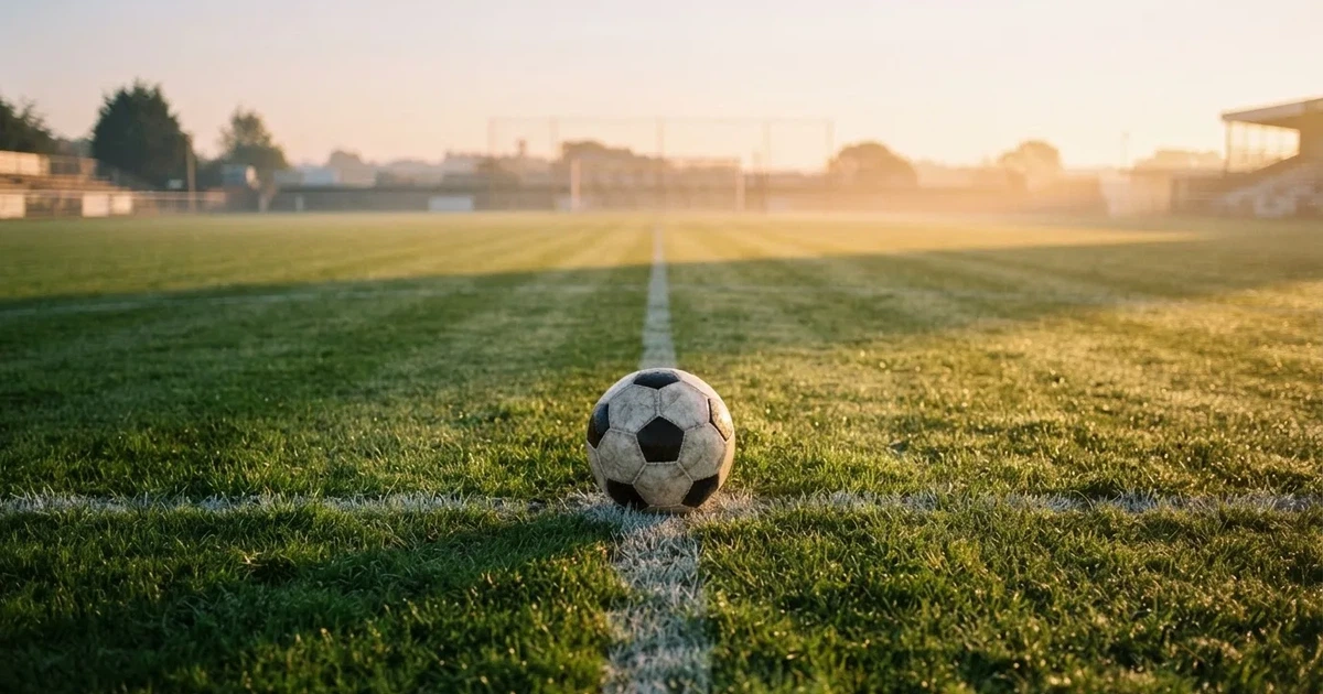 Een voetbal op de middenstip van een grasveld in het ochtendlicht
